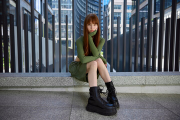 Young Woman in Green Dress Sitting Alone in Urban Setting, Modern Architecture