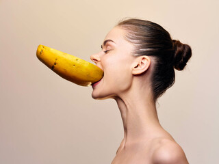 Woman holding banana in mouth while making eye contact with camera in front of her