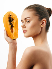 Portrait of a woman holding a fresh papaya in front of her face and smiling at the camera, tropical...