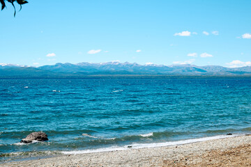 Obraz premium rocky shore of a blue lake, on the horizon a landscape of mountains with peaks covered with snow