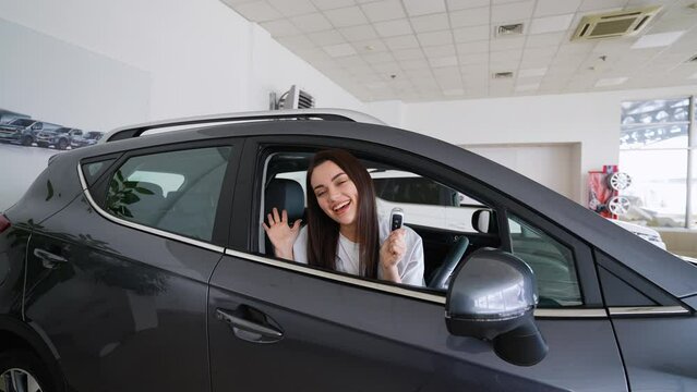 Happy woman holding keys to her new car at the dealership. Right hand drive car
