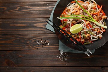 Shrimp stir fry with noodles and vegetables in wok on wooden table, top view. Space for text