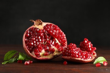 Cut fresh pomegranate and green leaves on wooden table