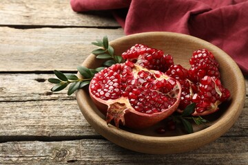 Cut fresh pomegranate and green leaves on wooden table. Space for text