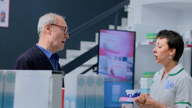 Aged client in need of prescription illness prevention drug informations in apothecary, asking experienced pharmacist. Pharmacy worker helping elderly customer with pharmaceutical expertise
