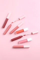 Different lip glosses and applicators on pink background, flat lay