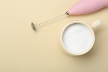 Mini mixer (milk frother) and cup of whipped milk on beige background, flat lay. Space for text