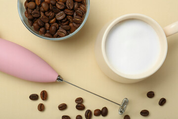 Mini mixer (milk frother), cup of whipped milk and coffee beans on beige background, flat lay