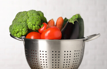 Fresh vegetables in colander on light background, closeup