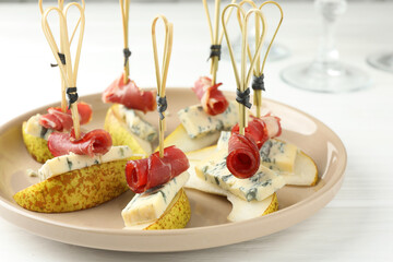 Tasty canapes with pears, blue cheese and prosciutto on white wooden table, closeup