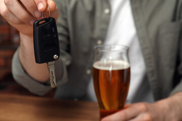 Man with glass of alcoholic drink holding car key, closeup. Don't drink and drive concept
