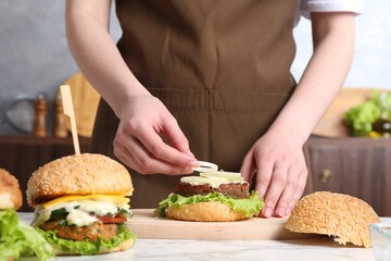 Woman making delicious vegetarian burger at white marble table, closeup