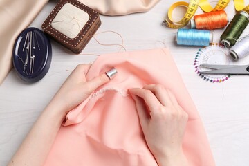 Woman with sewing needle and thread embroidering on cloth at white wooden table, top view
