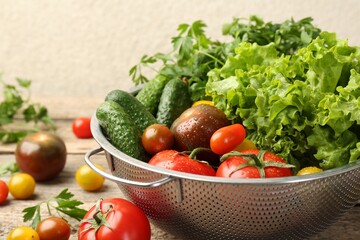 Wet vegetables in colander on wooden table, closeup