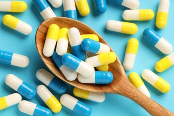 Many antibiotic pills with wooden spoon on light blue background, top view. Medicinal treatment