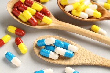 Many antibiotic pills with wooden spoons on grey background, closeup. Medicinal treatment