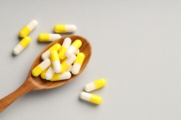 Many antibiotic pills with wooden spoon and space for text on grey background, top view. Medicinal...