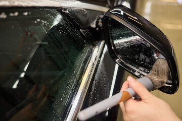 A person is cleaning a car windshield with a brush and water