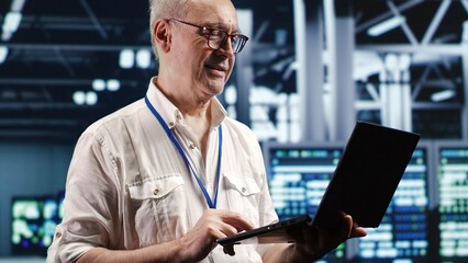 Proactive professional navigating network of server hardware in industrial hub. IT consultant with laptop doing optimizations and maintenance in data center, preventing system errors