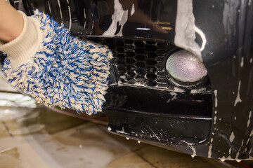 Person using blue glove for closeup car wash with brush and water