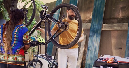 Young sports-loving multiracial couple repairing broken bicycle using professional equipment....