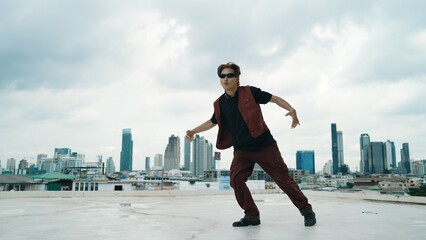 Motion shot of B-boy dance performance by professional street dancer at rooftop with sky scrapper,...