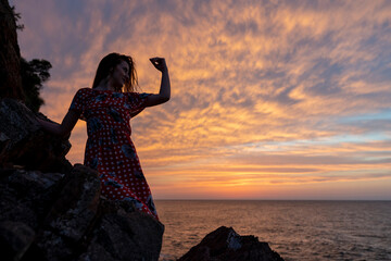 Silhouette of a lonely woman sitting on the rocks. A lonely woman watching the sea at sunset