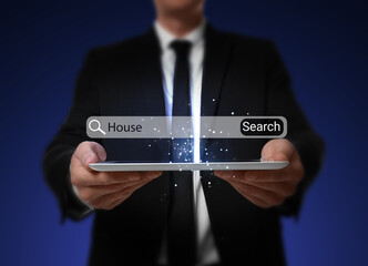 Real estate agent holding tablet on dark blue background, closeup. Virtual search bar with word House over device