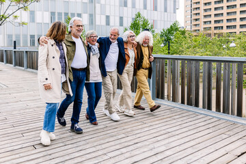 Senior group of retiree people having fun hugging each other while enjoying a walk at city street. Retirement and elderly friendship concept.
