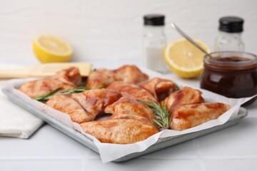 Raw marinated chicken wings and rosemary on light tiled table, closeup
