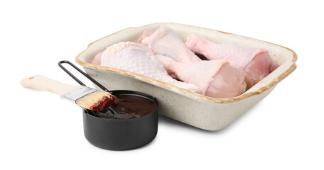 Raw chicken drumsticks in baking dish, marinade and basting brush isolated on white