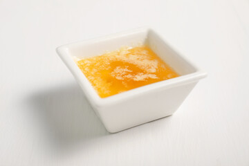 Melted butter in bowl on white wooden table, closeup
