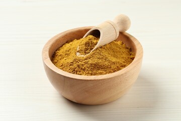 Dry curry powder in bowl and scoop on light wooden table, closeup