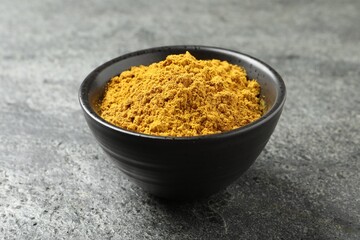 Dry curry powder in bowl on dark textured table, closeup