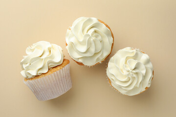 Tasty vanilla cupcakes with cream on beige background, top view