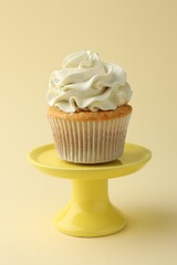 Tasty vanilla cupcake with cream on pale yellow background