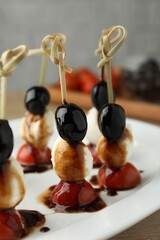 Tasty canapes with black olives, mozzarella and cherry tomatoes on table, closeup