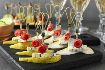 Tasty canapes with pears, blue cheese and prosciutto on grey table, closeup