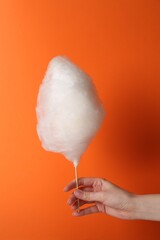 Woman holding sweet cotton candy on orange background, closeup