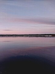 Obraz premium Realistic photo of the calm water surface at dusk, with distant reflections and a sky in shades of pink and purple. 