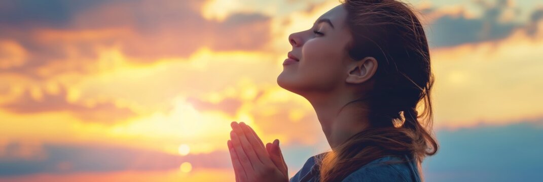 A woman is captured at sunset with hands clasped in prayer, the sun providing a peaceful backdrop