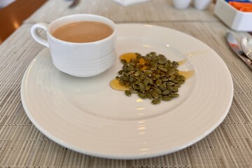 A cup of coffee sits beside a sound of pumpkin seeds poured with liquid lime honey, showcasing a contract between the liquid beverage and the solid ingredient at the table. Close-up