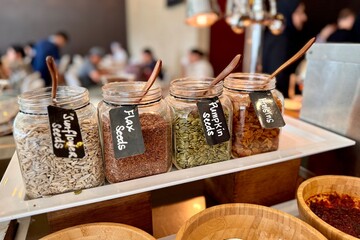 Large transparent glass jars with wooden spoons for a set of flax seeds, pumpkin seeds, sunflower seeds and raisins are served at the buffet restaurant during meals