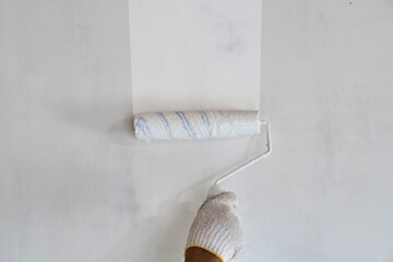 Painter hand holding roller brush painting new white wall, diy interior exterior home renovation