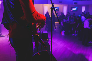 Concert view of an electric guitar player with vocalist and rock band performing in a club, male musician guitarist on stage with audience in a crowded concert hall arena, hands on a bass guitar
