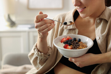 Woman eating tasty granola with fresh berries and yogurt at home, closeup