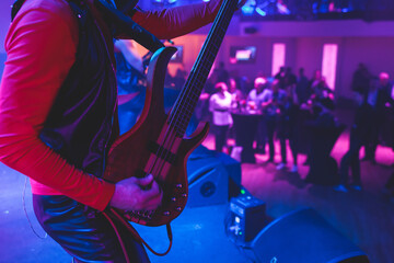 Concert view of an electric guitar player with vocalist and rock band performing in a club, male...