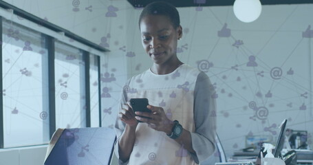 Image of connected icons over african american woman using cellphone in office - Powered by Adobe