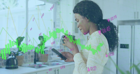 Image of graphs with changing numbers, biracial woman scrolling on cellphone while drinking tea