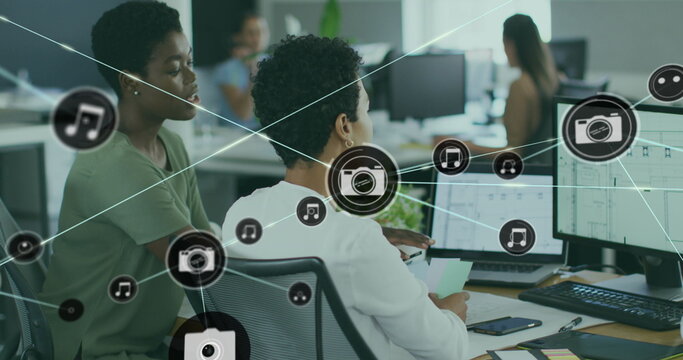 Image of connected icons over diverse female coworkers discussing reports on computer